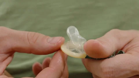 Hands Unrolling a Condom Slightly While Preparing It for Use, Emphasizing Safe Stock Footage 301025839