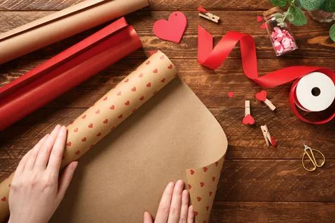 Hands unrolling heart-patterned craft paper on wooden table. Gift wrapping .. Stock Photos