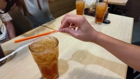 Hands Unwrapping a Drinking Straw Over Iced Tea in Bangkok Stock Footage 343367178