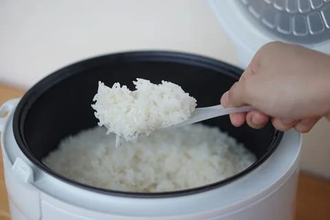 Hands use a plastic spoon to scoop rice from the electric rice cooker. Concept,  Stock Photos