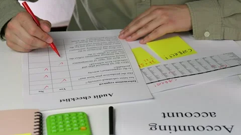 Hands use a red marker to check off items on an audit checklist alongside Stock Footage 316296903
