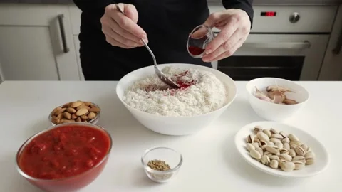 Hands use a spoon to fold bright red seasoning into uncooked white rice in .. Stock Footage 332159834
