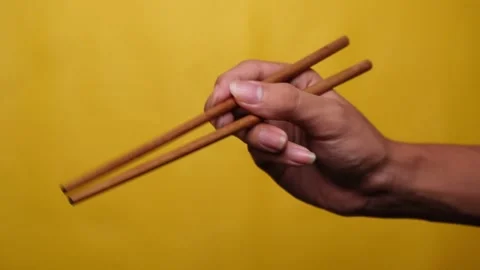 Hands using chopsticks on an isolated yellow background Stock Footage 275872483
