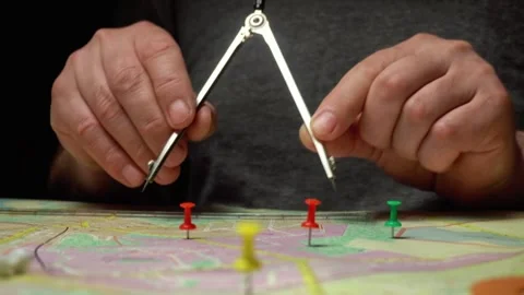 Hands using a compass to measure distances on a colorful map with multiple push Stock Footage 332649398
