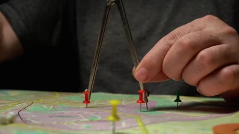 Hands using compass to measure distances on a map with colorful push pins placed Stock Footage 333146574