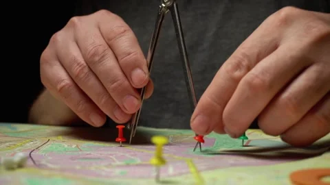 Hands using compass to measure distances on a map with colorful push pins placed Stock Footage 333240020