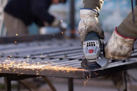 Hands using a cordless angle grinder to fix a metal fence Stockfoto's
