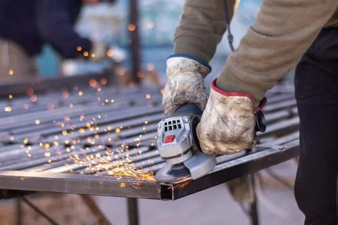 Hands using a cordless angle grinder to fix a metal fence Stock Photos