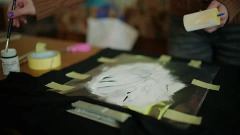 Hands using a craft roller to evenly spread adhesive material over a stencil Видео 336893093