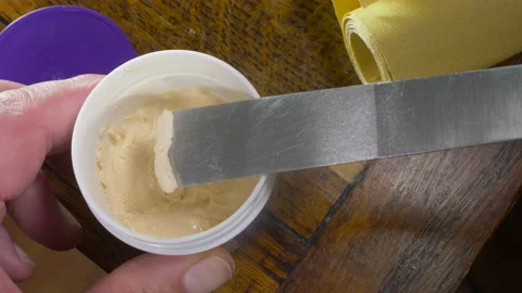 Hands using flat knife to take wood filler from tub for table repair. Video stock 155959637