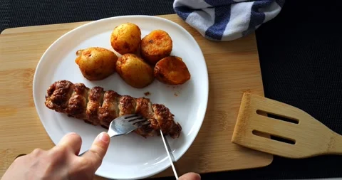 Hands using fork and knife cutting a piece of delicious grilled kebab served Stock Footage 316756232