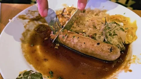 Hands using fork and knife to slice bratwurst sausage served with sauerkraut Stock Footage 335989735