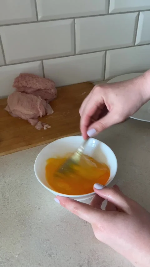 Hands using fork to beat raw eggs in white bowl on countertop with pieces of raw Stock Footage 311511687