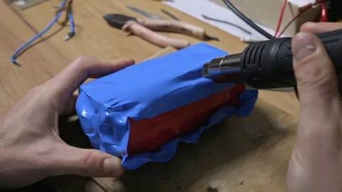 Hands Using Heat Gun to Shrink Blue PVC Wrap on Lithium Battery Pack 스톡 동영상 329908775