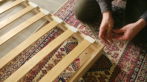 Hands using hex key to secure bolts on wooden bed frame, emphasizing creative Stock Footage 312848046