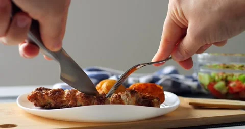 Hands using knife and fork cutting a piece of grilled chicken breast served with Stock Footage 316757290