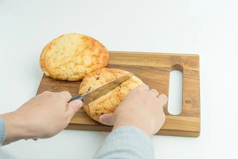 Hands using a knife to slice a fresh golden bread bun on a wooden board Stock Photos