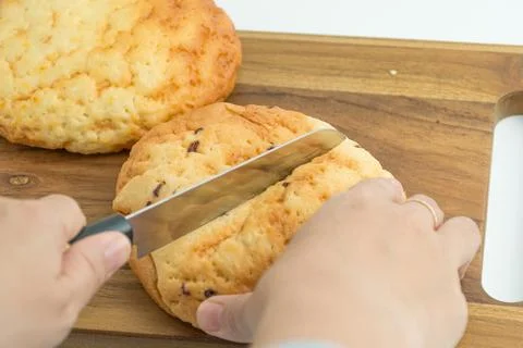 Hands using a knife to slice a fresh golden bread bun on a wooden board Stock Photos
