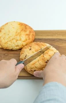 Hands using a knife to slice a fresh golden bread bun on a wooden board Foto stock