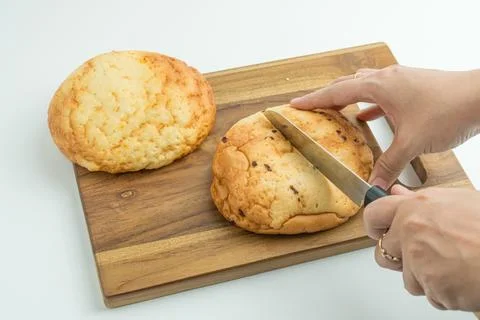Hands using a knife to slice a fresh golden bread bun on a wooden board Foto stock