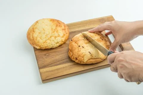 Hands using a knife to slice a fresh golden bread bun on a wooden board Foto stock