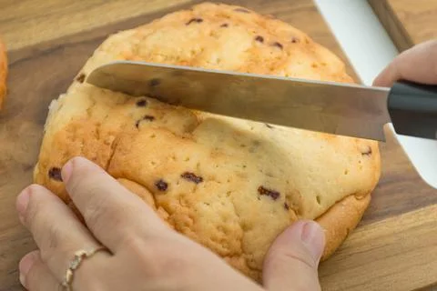 Hands using a knife to slice a fresh golden bread bun on a wooden board Stock Photos