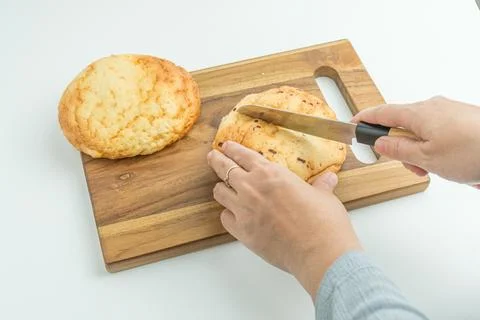 Hands using a knife to slice a fresh golden bread bun on a wooden board Stock Photos
