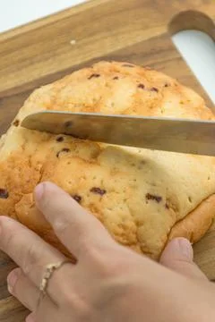 Hands using a knife to slice a fresh golden bread bun on a wooden board Foto stock
