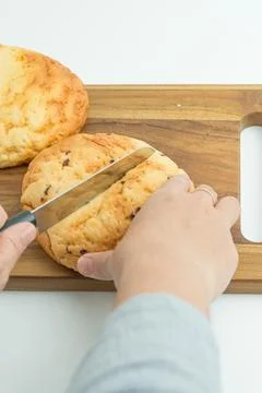Hands using a knife to slice a fresh golden bread bun on a wooden board Foto stock