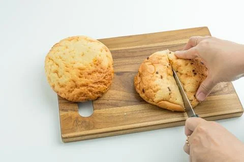 Hands using a knife to slice a fresh golden bread bun on a wooden board Foto stock