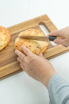 Hands using a knife to slice a fresh golden bread bun on a wooden board Foto stock
