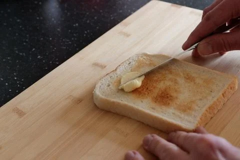 Hands using knife to spread butter on toast Stock Photos