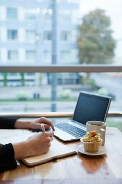 Hands using laptop and notebook with cup of tea and cake on wooden table in c Stock Photos