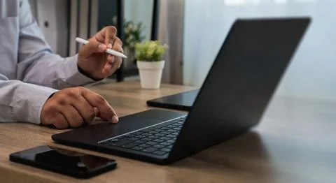 Hands using laptop keyboard and stylus on desk with smartphone and plant, i.. 스톡 사진