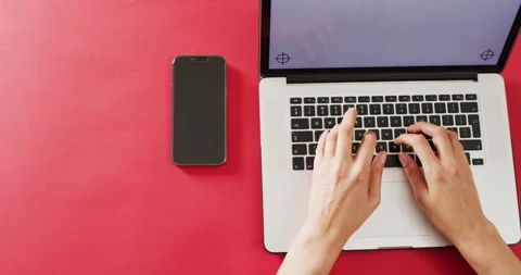 Hands using laptop with smartphone on red desk with copy space Stock Footage 343511991