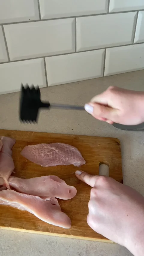 Hands using meat mallet to pound raw chicken fillet on wooden cutting board in Stock Footage 311511140