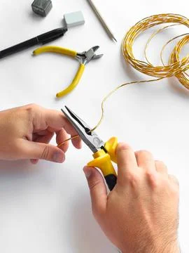 Hands using pliers to trim wire with tools on white surface for diy project Foto stock