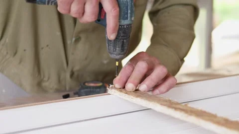 Hands using power drill to fasten narrow wooden strip on white work surface Stock Footage 344873353