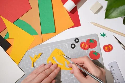 Hands using a precision knife to cut cheese shapes from yellow paper on a g.. Stock Photos