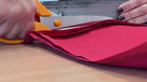 Hands using scissors to cut red fabric on wooden table surface Vídeos de archivo 343679860