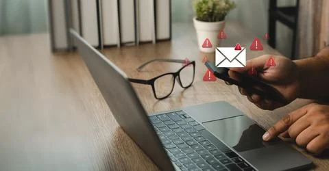 Hands using a smartphone beside a laptop with email envelope and warning ic.. Stock Photos