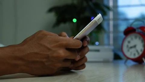 Hands using smartphone beside red alarm clock, Close-up of hands using a sm.. Stock Footage 345119467