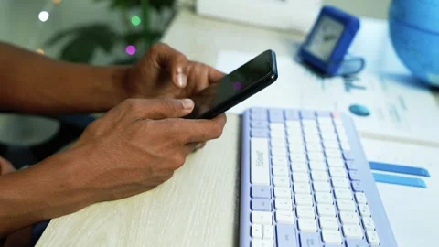 Hands using a smartphone beside a white keyboard and printed business chart.. Video stock 345119015