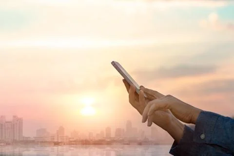 Hands using smartphone on city at sunset background Photos