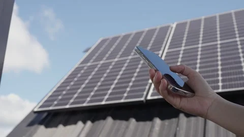 Hands using smartphone to control electricity usage with solar panels on rooftop Stock Footage 326085170