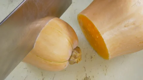 Hands using a steel cleaver to cut a raw butternut squash vegetable. Stock-Footage 143843045