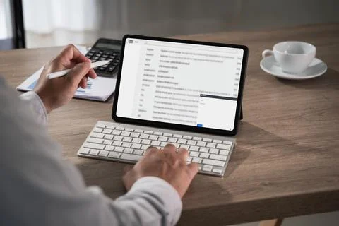 Hands using tablet displaying email inbox with keyboard on desk alongside c.. Stock Photos