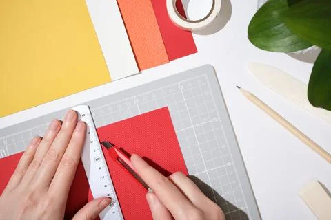 Hands using utility knife and ruler to cut red paper on cutting mat. Workspac 库存照片