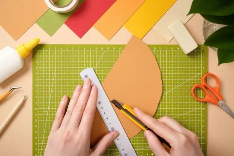 Hands using utility knife and ruler to cut colored paper on green cutting mat Stock Photos