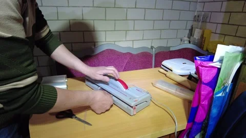Hands using a vacuum sealer to package food items on a table in a kitchen settin Stock-Footage 332453593